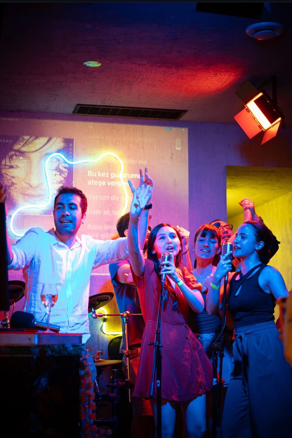 Group of people singing karaoke at Teddy Beer bar with colorful neon lights