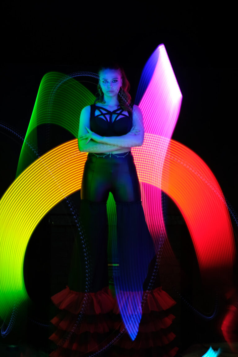 Performer standing in front of vibrant LED light trails during a night event at Teddy Beer